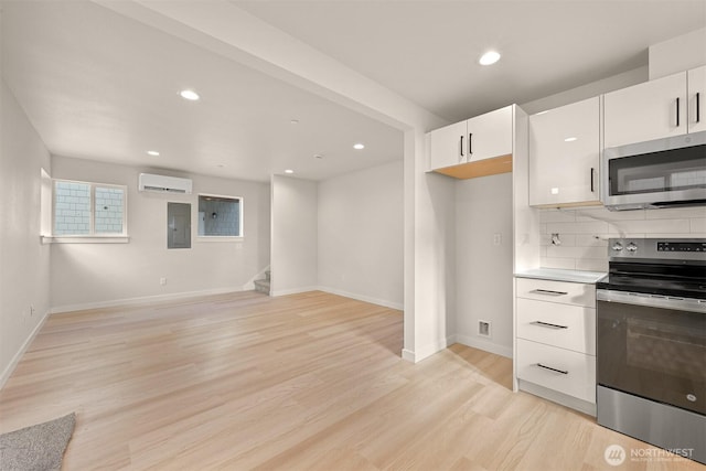 kitchen with a wall mounted AC, light wood-style flooring, electric panel, appliances with stainless steel finishes, and white cabinetry