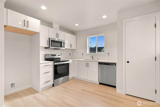 kitchen featuring a sink, backsplash, white cabinetry, and stainless steel appliances