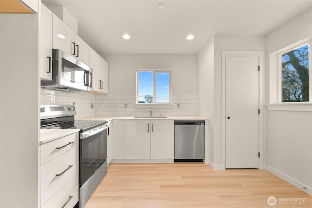 kitchen with backsplash, appliances with stainless steel finishes, light countertops, and a sink