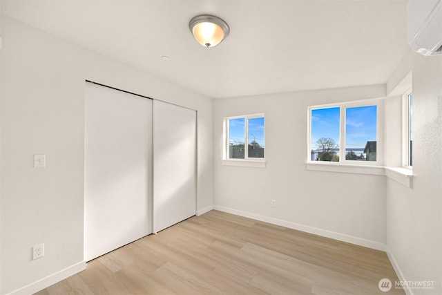 unfurnished bedroom with a closet, baseboards, light wood-style flooring, and a wall unit AC