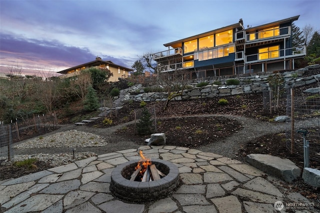 patio terrace at dusk featuring a fire pit, a balcony, and stairs