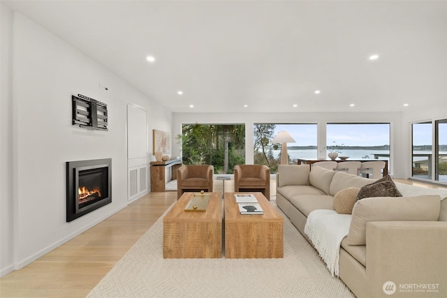 living area featuring a glass covered fireplace, recessed lighting, and light wood-style floors