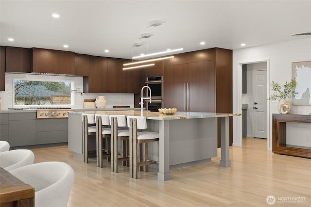 kitchen with modern cabinets, light wood-style flooring, a breakfast bar, tasteful backsplash, and stainless steel appliances