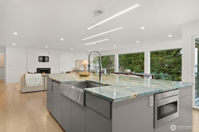 kitchen with stainless steel microwave, gray cabinetry, a lit fireplace, a large island with sink, and modern cabinets