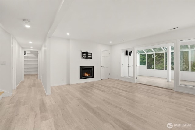 unfurnished living room with light wood-style flooring, visible vents, and a lit fireplace