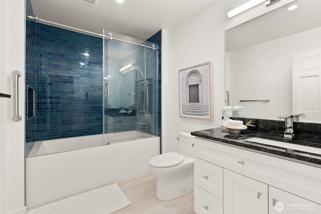 bathroom featuring combined bath / shower with glass door, toilet, wood finished floors, and vanity