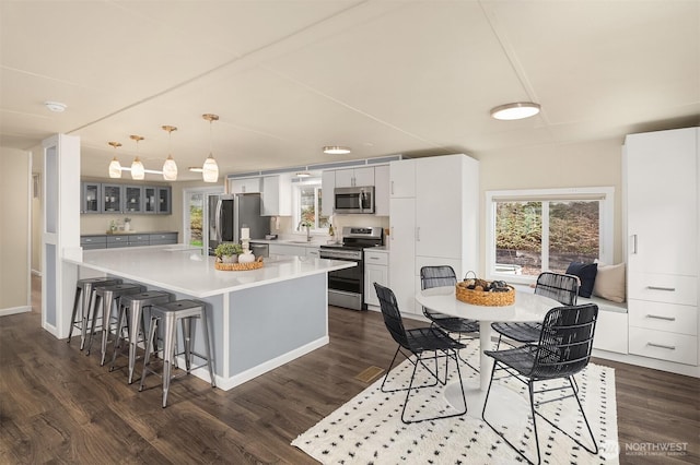 kitchen with dark wood finished floors, appliances with stainless steel finishes, glass insert cabinets, and a kitchen breakfast bar