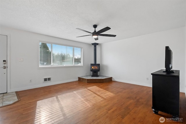 unfurnished living room with a wood stove, wood finished floors, visible vents, and a textured ceiling