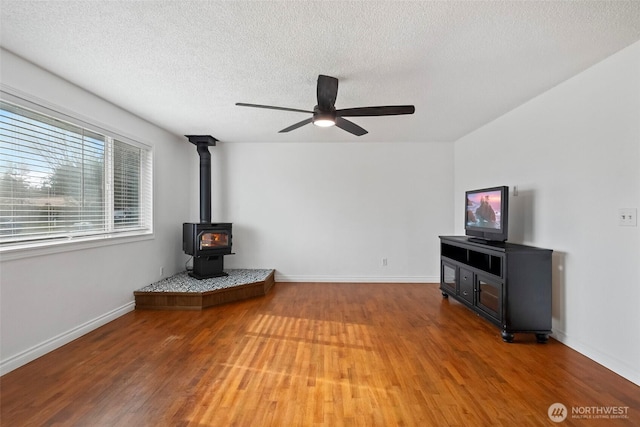 unfurnished living room with light wood-style flooring, a textured ceiling, baseboards, ceiling fan, and a wood stove