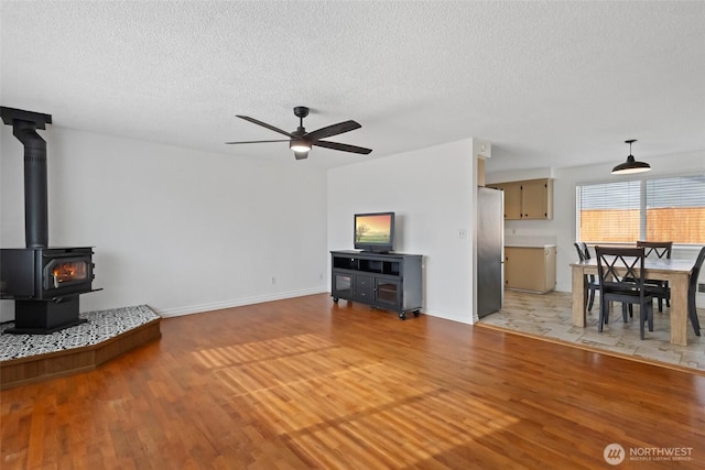 living room with light wood-type flooring, a ceiling fan, a wood stove, and a textured ceiling