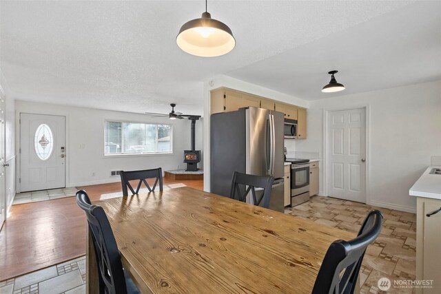 dining space featuring ceiling fan, a wood stove, baseboards, and a textured ceiling