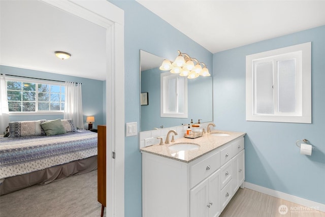 full bathroom featuring a sink, baseboards, double vanity, and ensuite bathroom