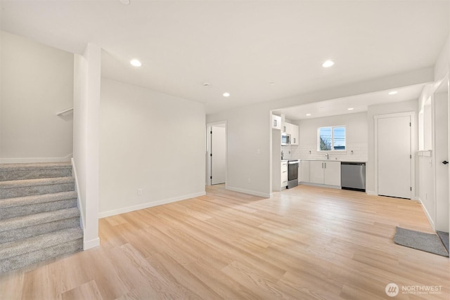 unfurnished living room featuring light wood-type flooring, stairway, baseboards, and recessed lighting