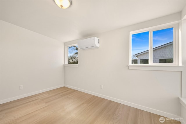 unfurnished room with light wood-type flooring, baseboards, and a wall mounted AC