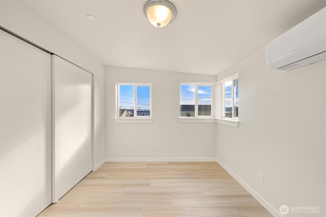 empty room with a wall mounted air conditioner, baseboards, and light wood finished floors