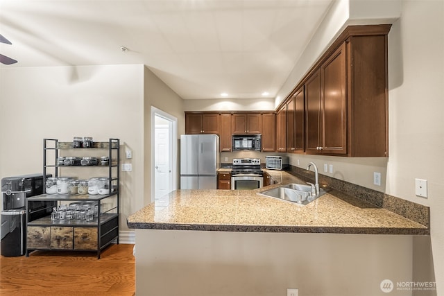 kitchen featuring wood finished floors, stone counters, a peninsula, a sink, and appliances with stainless steel finishes