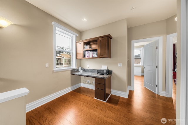 office area featuring baseboards, wood finished floors, and built in desk