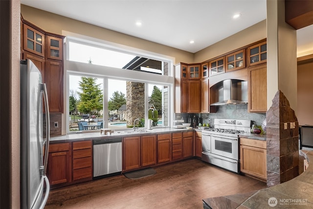 kitchen with dark wood finished floors, a sink, stainless steel appliances, wall chimney range hood, and tasteful backsplash