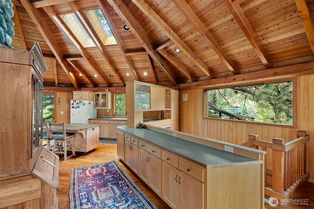 kitchen with vaulted ceiling with skylight, wood walls, a center island, and freestanding refrigerator