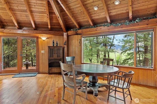 dining space with lofted ceiling with beams, a wealth of natural light, wooden walls, and light wood-style flooring