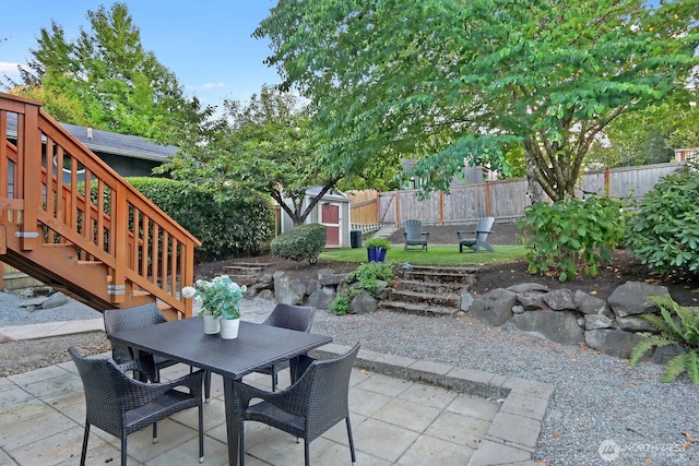 view of patio / terrace with an outbuilding, outdoor dining area, fence, and a shed