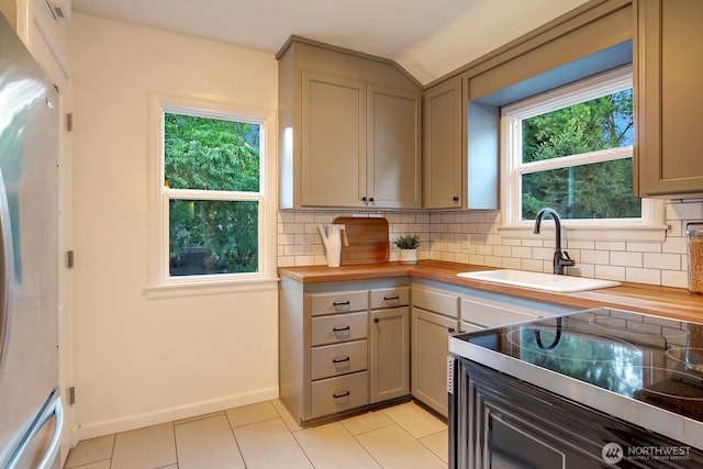 kitchen featuring butcher block counters, light tile patterned floors, decorative backsplash, freestanding refrigerator, and a sink