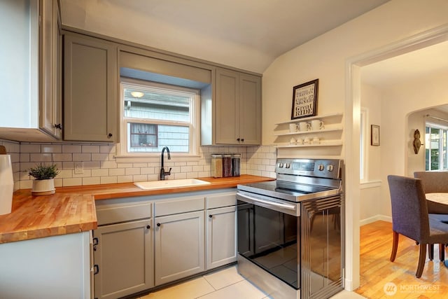 kitchen with wooden counters, plenty of natural light, arched walkways, electric range, and a sink