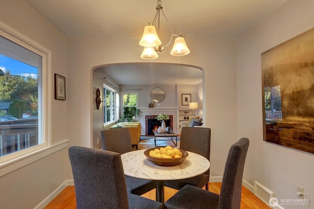 dining space featuring a notable chandelier, arched walkways, light wood-style floors, a fireplace, and baseboards