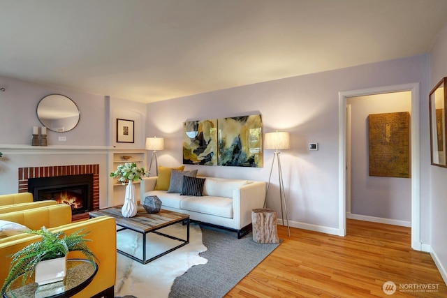 living room with baseboards, a brick fireplace, and wood finished floors