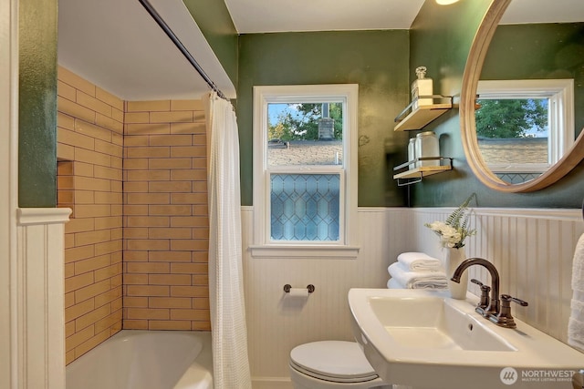 bathroom with a sink, toilet, shower / bath combo, and wainscoting