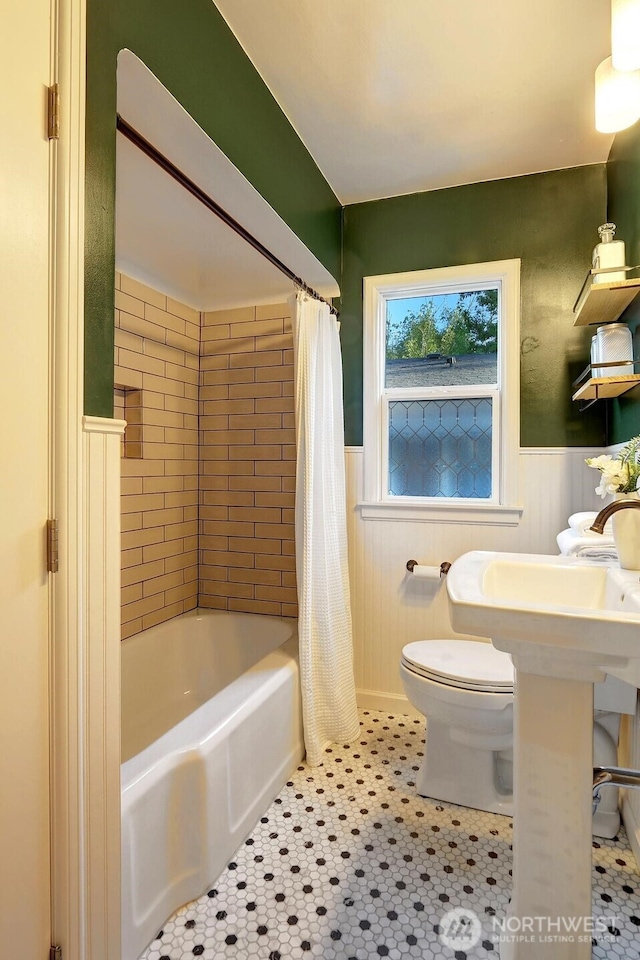 bathroom featuring tile patterned floors, a wainscoted wall, shower / bath combination with curtain, and toilet