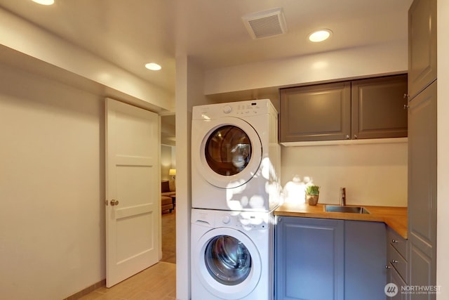 laundry area with visible vents, a sink, stacked washing maching and dryer, recessed lighting, and cabinet space