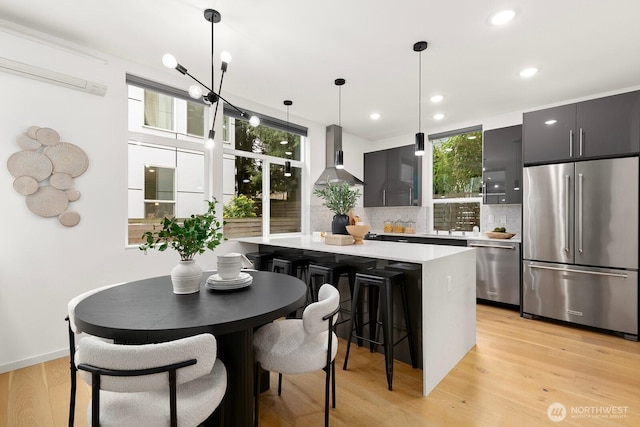 kitchen with wall chimney range hood, a wall mounted air conditioner, light countertops, light wood-style flooring, and stainless steel appliances