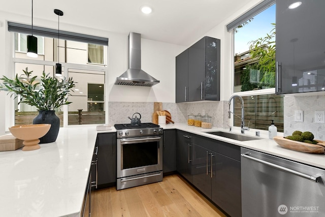 kitchen with stainless steel appliances, wall chimney exhaust hood, light countertops, and a sink