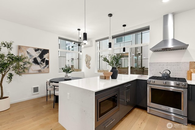 kitchen featuring decorative backsplash, light wood-style flooring, wall chimney exhaust hood, and stainless steel appliances