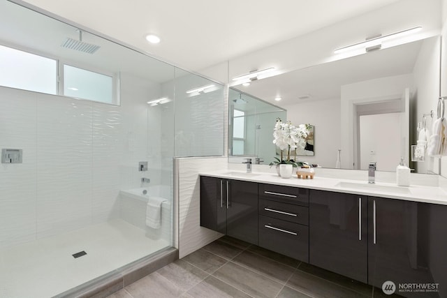 bathroom with double vanity, visible vents, a tile shower, and a sink