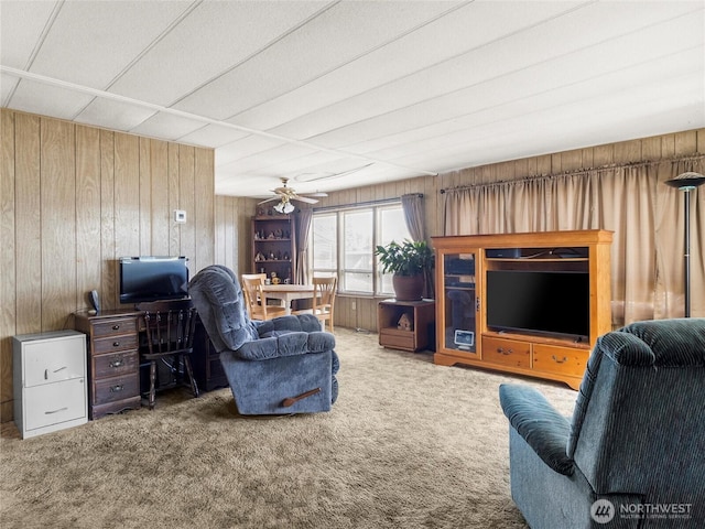 carpeted living room with ceiling fan and wood walls