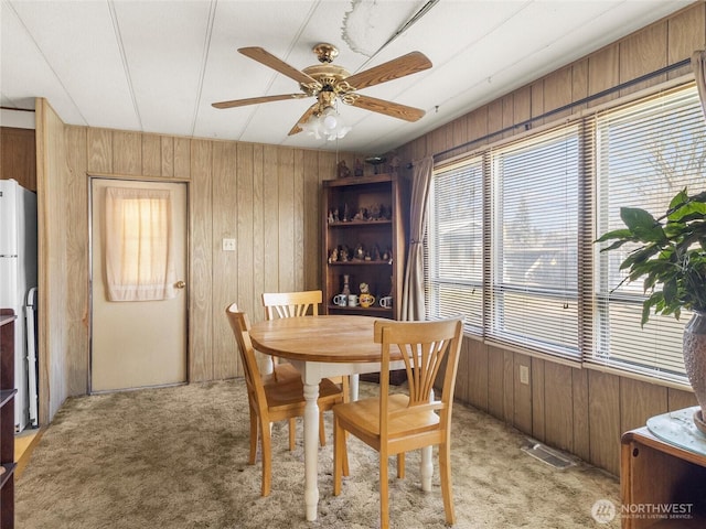 dining space with light colored carpet, visible vents, wood walls, and ceiling fan