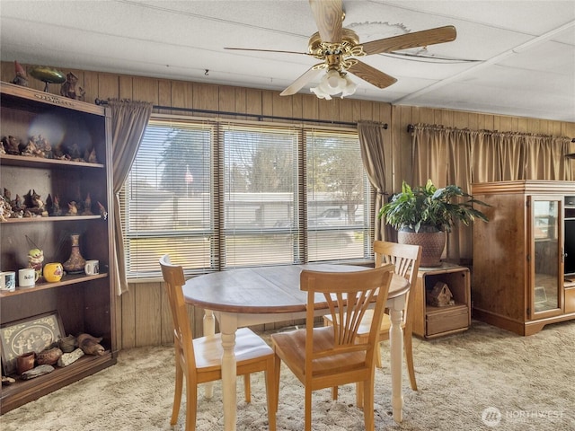 dining room featuring wooden walls, light colored carpet, and ceiling fan