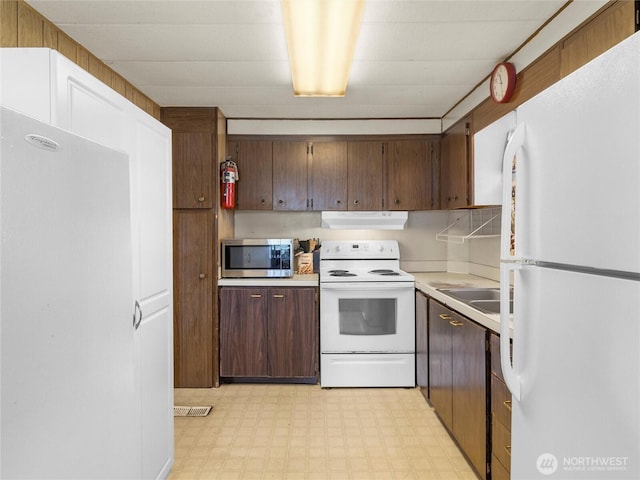 kitchen with white appliances, light floors, a sink, light countertops, and under cabinet range hood