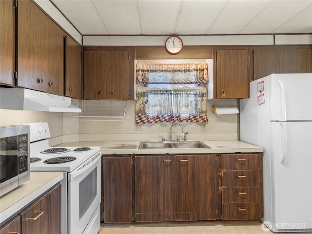 kitchen featuring under cabinet range hood, a sink, white appliances, light countertops, and light floors