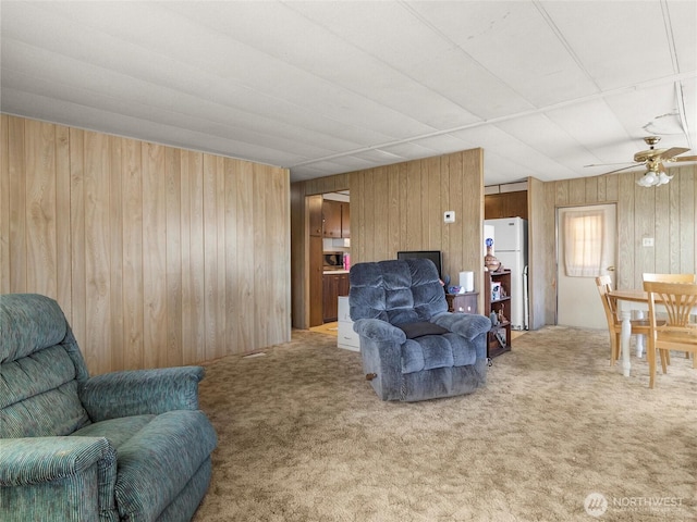 living area with light carpet, wood walls, and ceiling fan