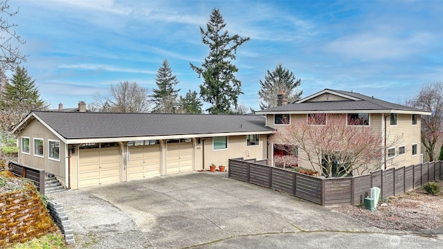 tri-level home featuring central air condition unit, driveway, a chimney, and fence