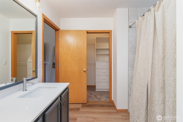 bathroom with curtained shower, vanity, a walk in closet, and wood finished floors