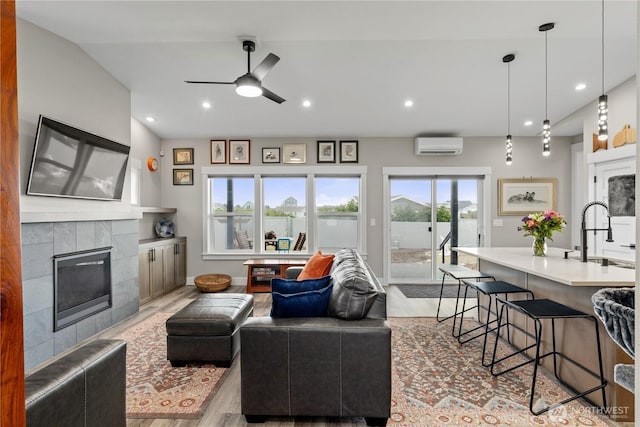 living room with ceiling fan, a tiled fireplace, a wall mounted air conditioner, recessed lighting, and light wood-style flooring