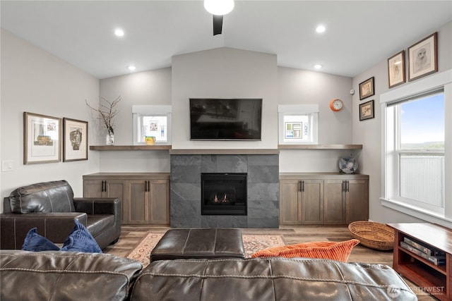 living room with a tiled fireplace, plenty of natural light, lofted ceiling, and wood finished floors