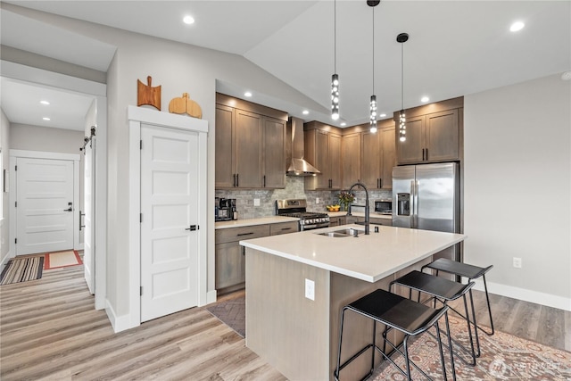 kitchen with a sink, wall chimney range hood, stainless steel appliances, light wood finished floors, and light countertops