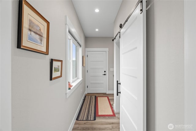 hall featuring a barn door, recessed lighting, baseboards, and light wood-type flooring