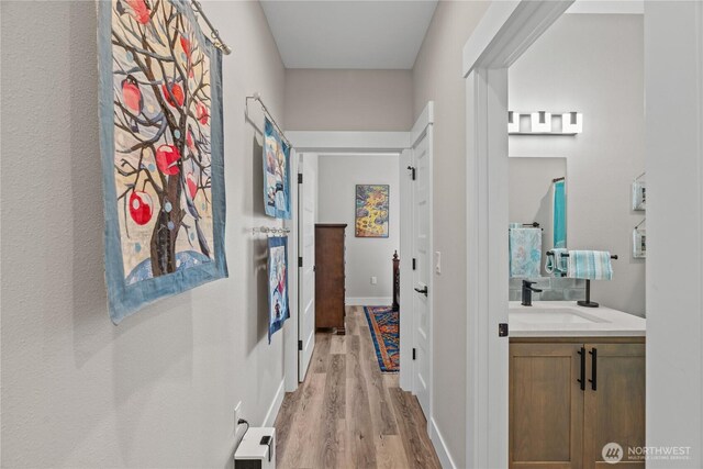 corridor with light wood-style flooring, baseboards, visible vents, and a sink