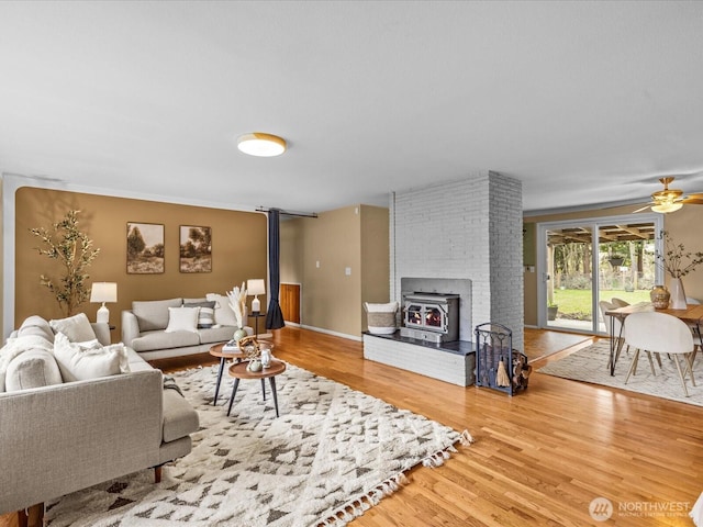 living area with a wood stove, a ceiling fan, and wood finished floors